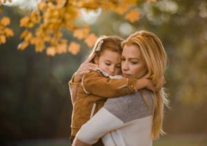 Affectionate mother consoling her little girl during autumn day in nature.